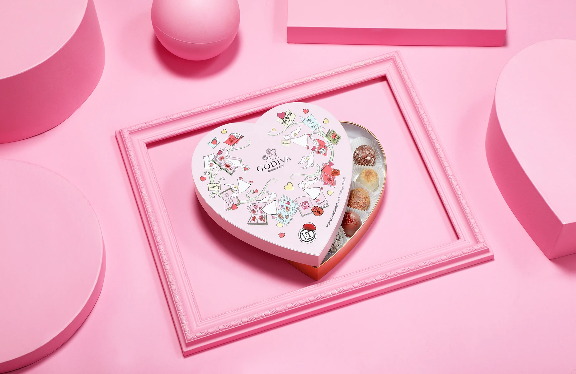 Advertising product photography of a heart-shaped Godiva chocolate gift box styled on a pink geometric set.