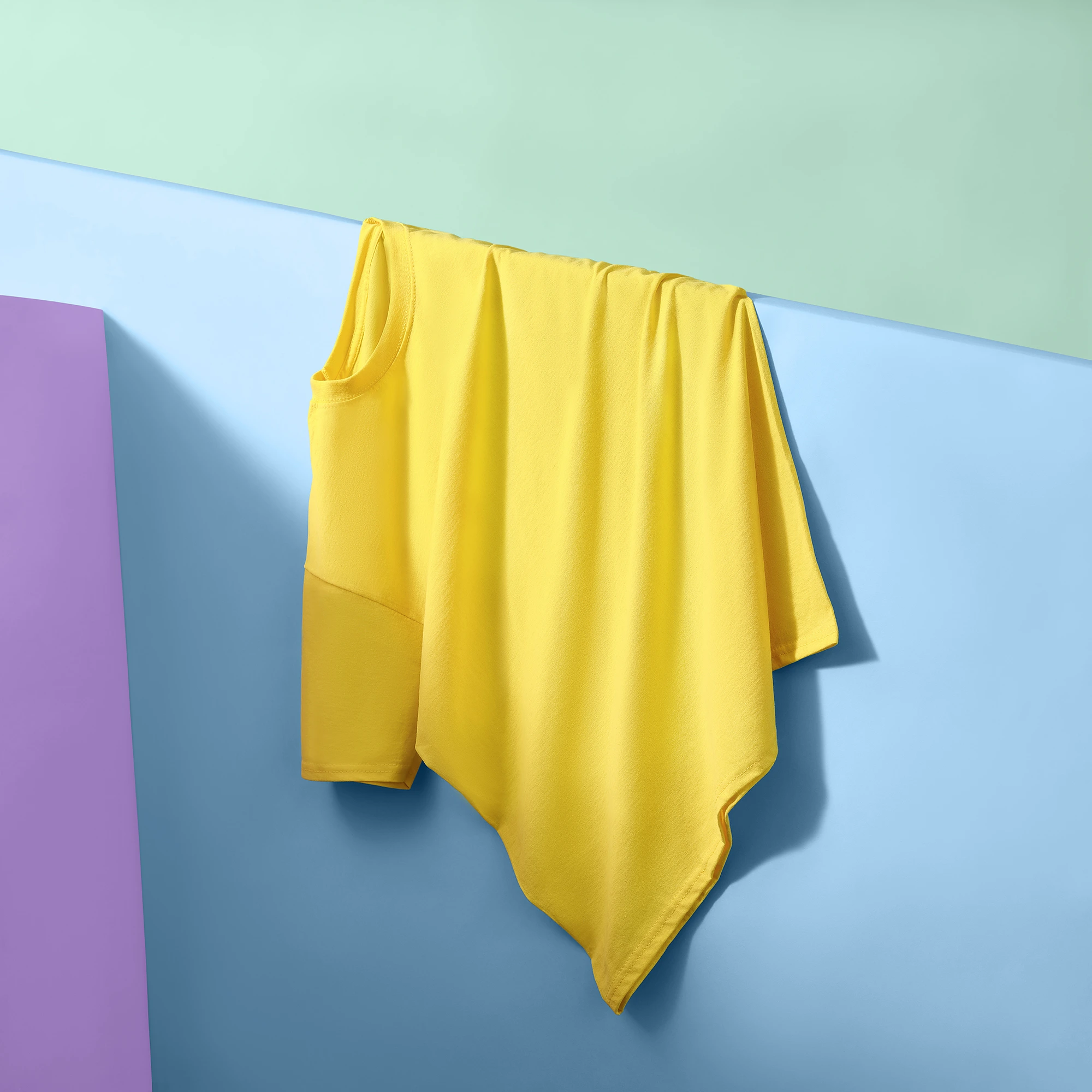 Commercial fashion photography of a yellow T-shirt draped over a blue geometric set with pastel backgrounds at a London photography studio.