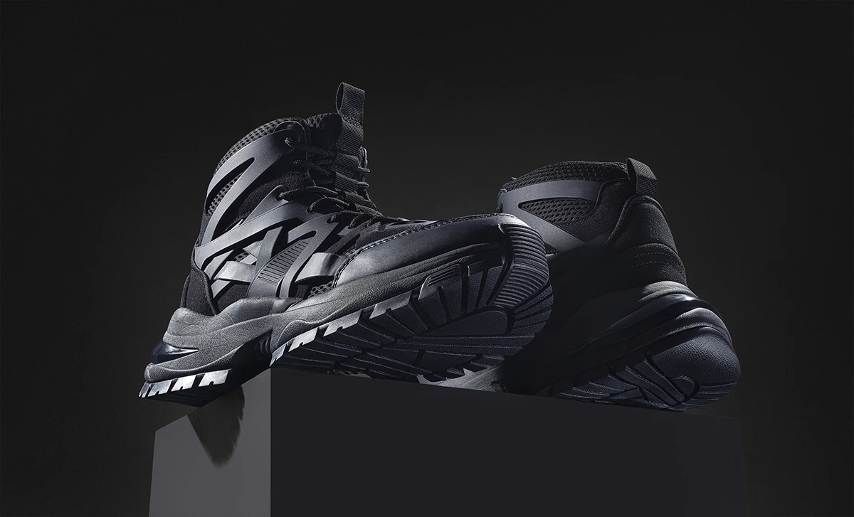 Studio product photography of black high-top trainers displayed on a pedestal against a dark background.