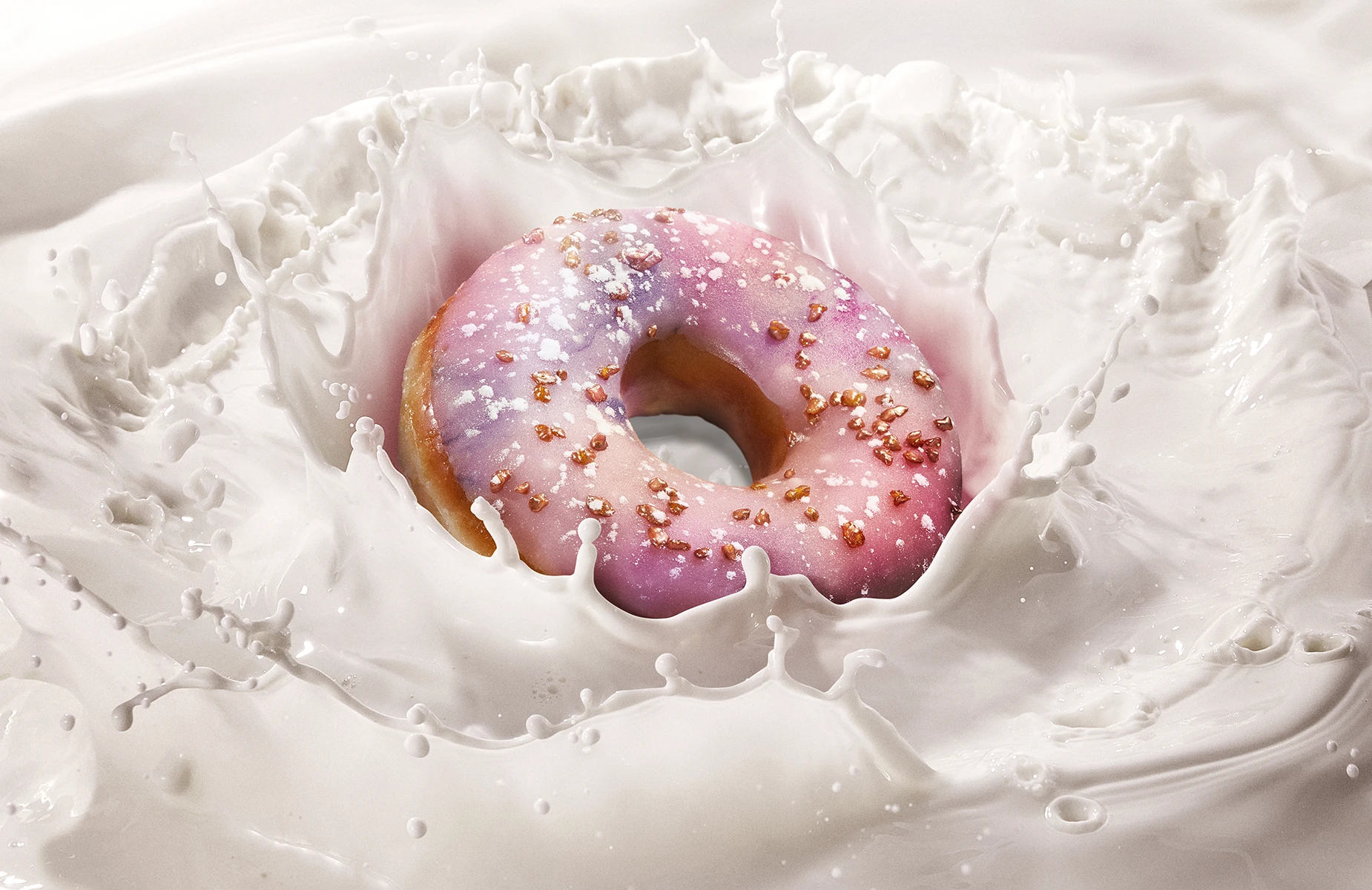 Creative food photography of a pink-glazed doughnut landing in a splash of milk.