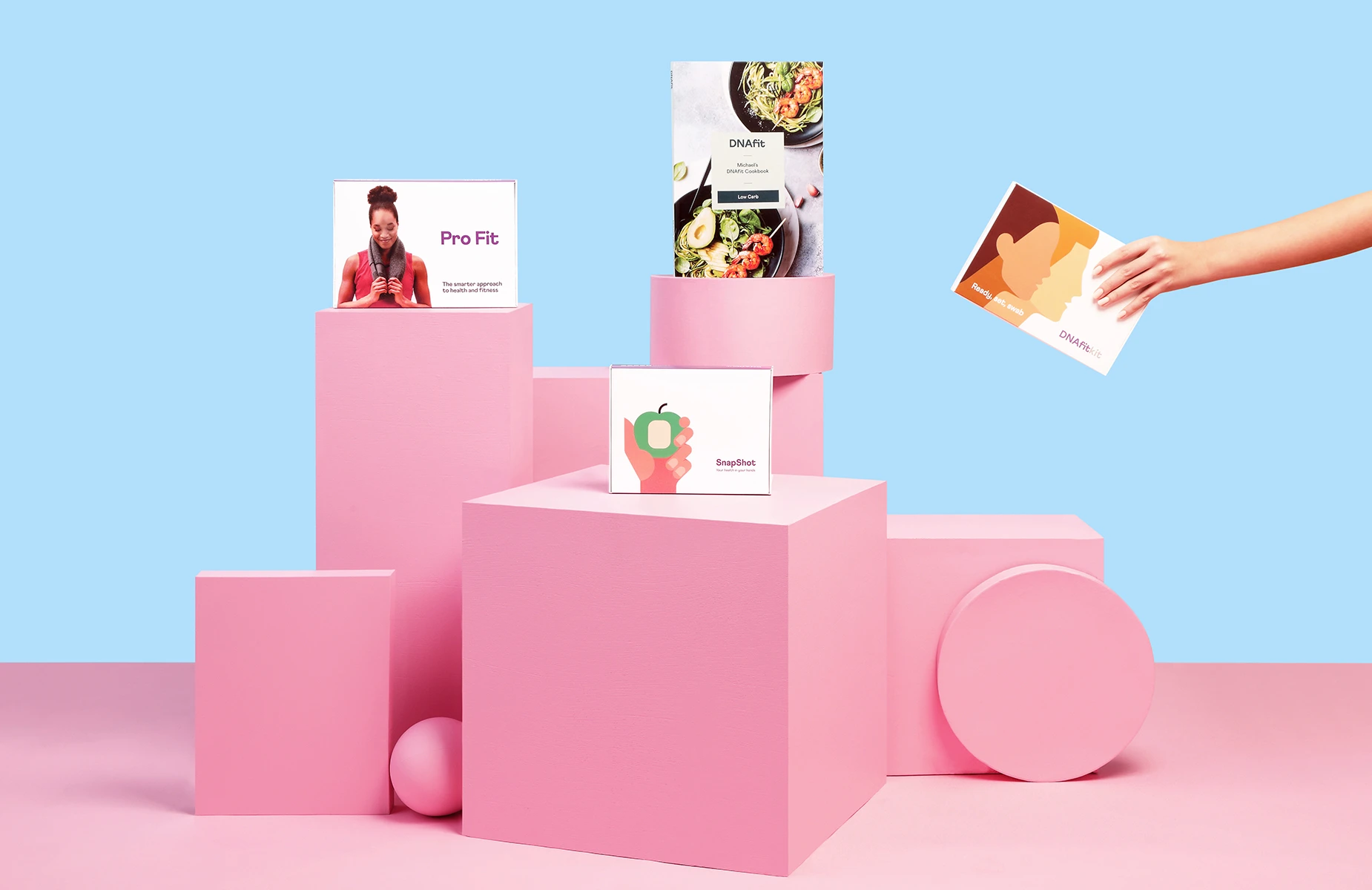 Advertising product photography of DNAfit health and nutrition kits displayed on pink geometric plinths.